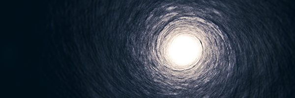 The inside of a dark tunnel with light at the end of it.